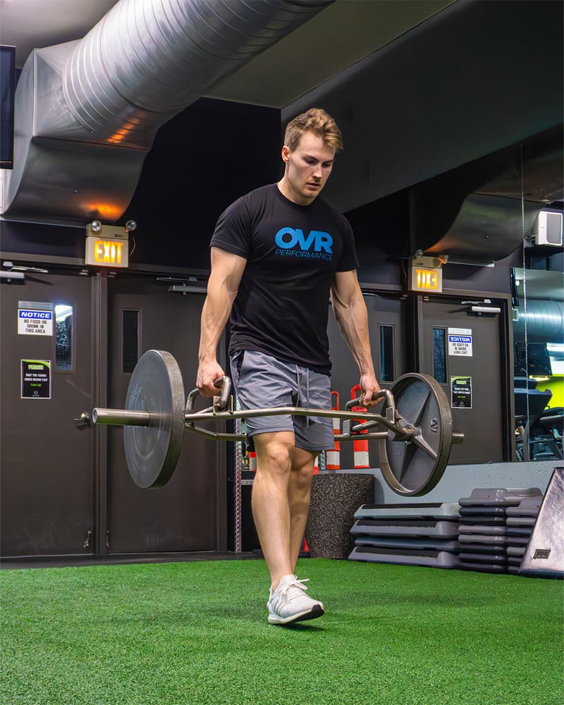 Adam carrying a loaded trap bar through a gym